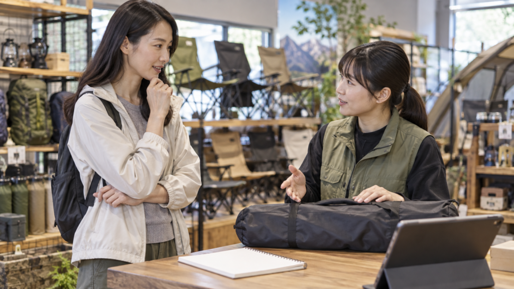 成人女性がキャンプ椅子の使用場所と試座条件を販売店で相談する様子
