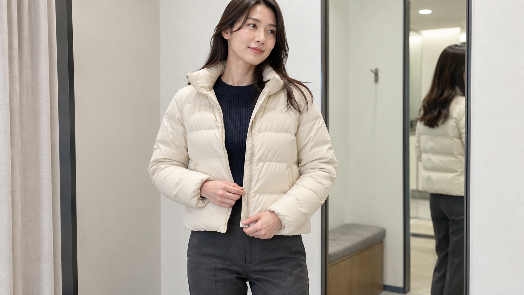 ネイビーのニットに白い短丈ダウンを重ね、前を閉めようとする女性