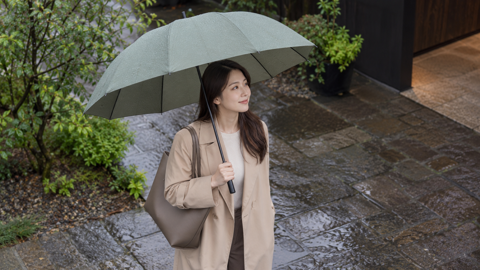 肩掛けバッグと体の位置を傘の下で確認する女性のイメージ